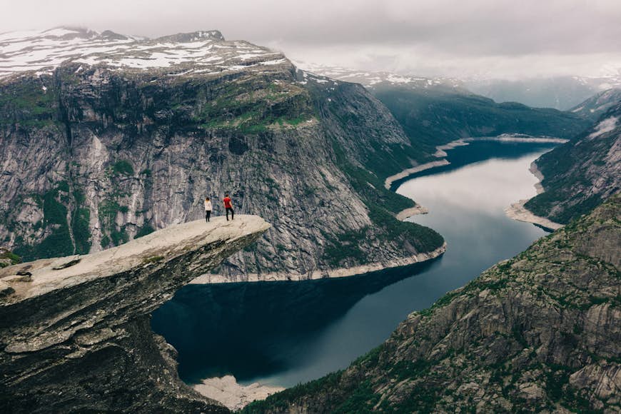 Two people standing on the Trolltunga, a large ledge of rock that juts out high above a fjord in Norway