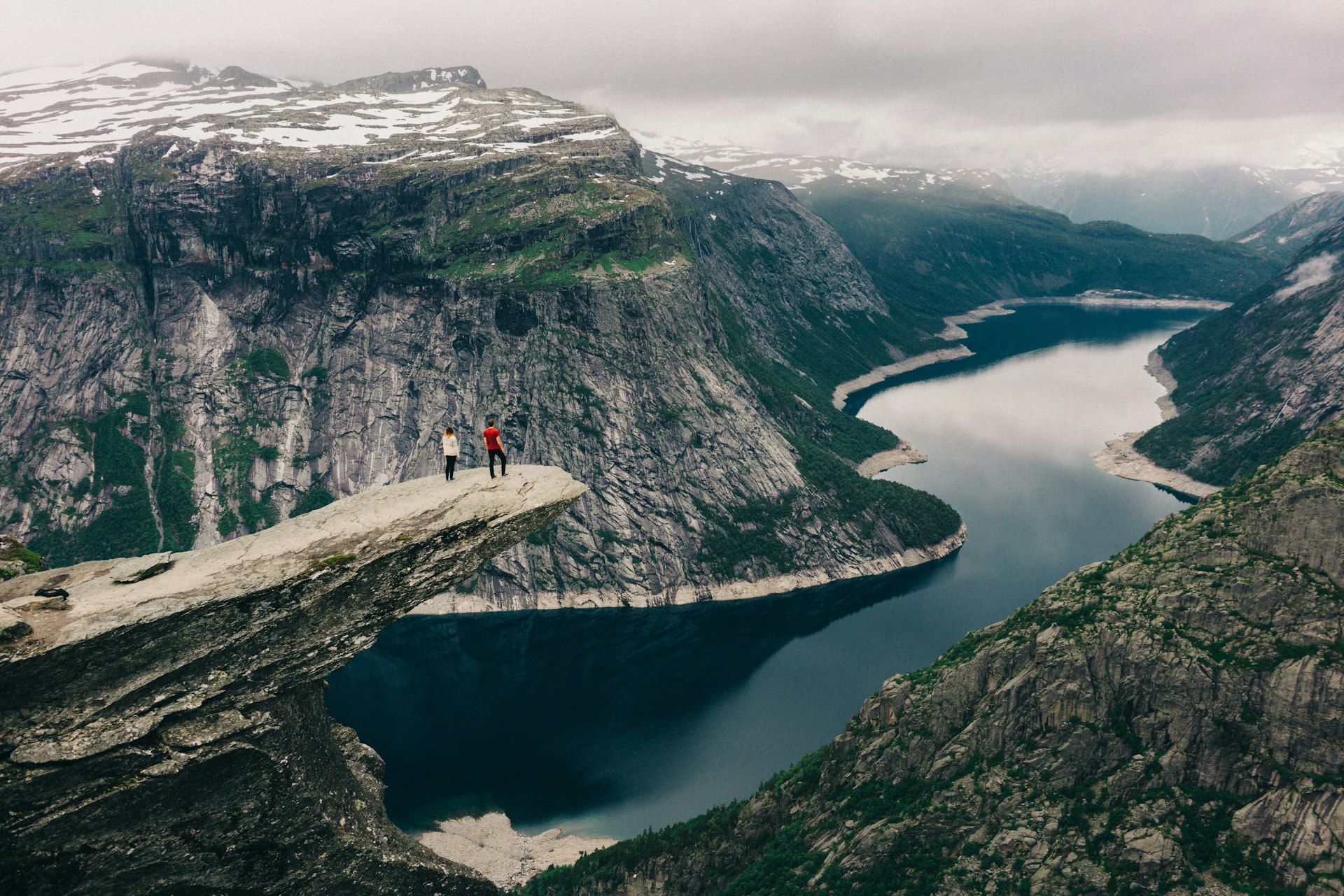 Two people standing on the Trolltunga, a large ledge of rock that juts out high above a fjord in Norway
