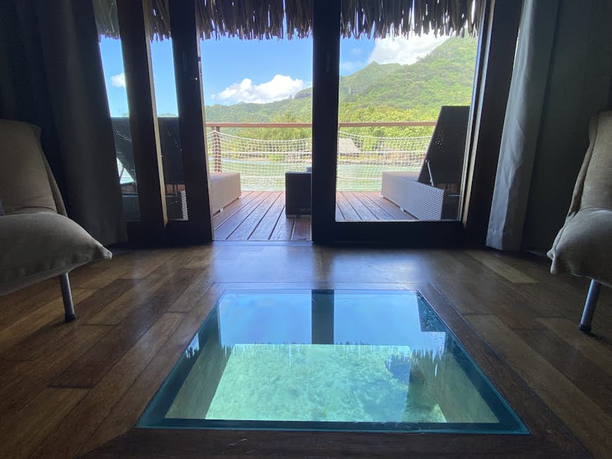 The interior of an overwater bungalow, complete with a view of the ocean below