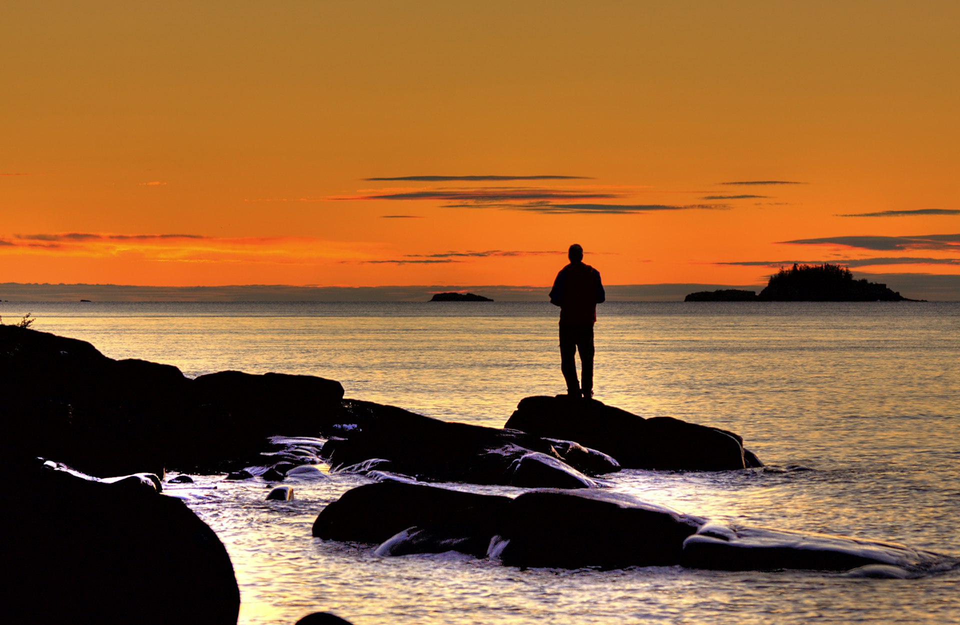 Man standing on a rocky outcrop watches the red sky of a sunrise over Lake Superior at Isle Royale National Park in Michigan