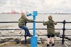 Two little boys using a telescope to look at the view of Liverpool across the The river Mersey from New Brighton