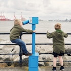 Two little boys using a telescope to look at the view of Liverpool across the The river Mersey from New Brighton