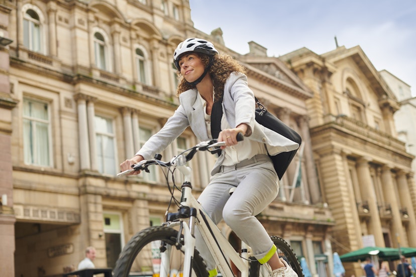 A young woman in a light gray suit cycles through Liverpool city center