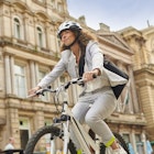 A young woman in a light gray suit cycles through Liverpool city center