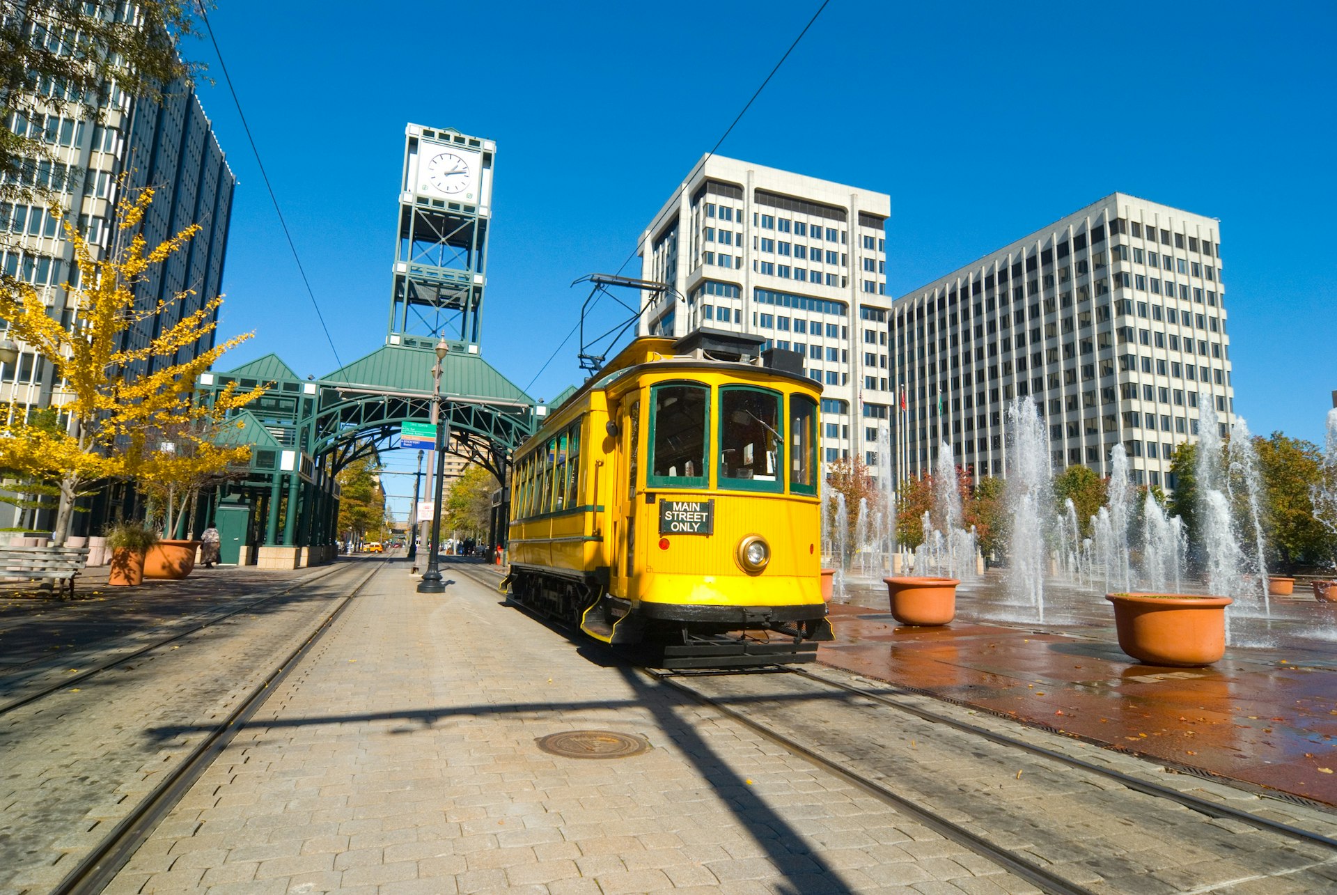 "The Historic Main Street Trolley in Memphis, Tennessee, with buildings, an elegant station, and water fountains in the background.