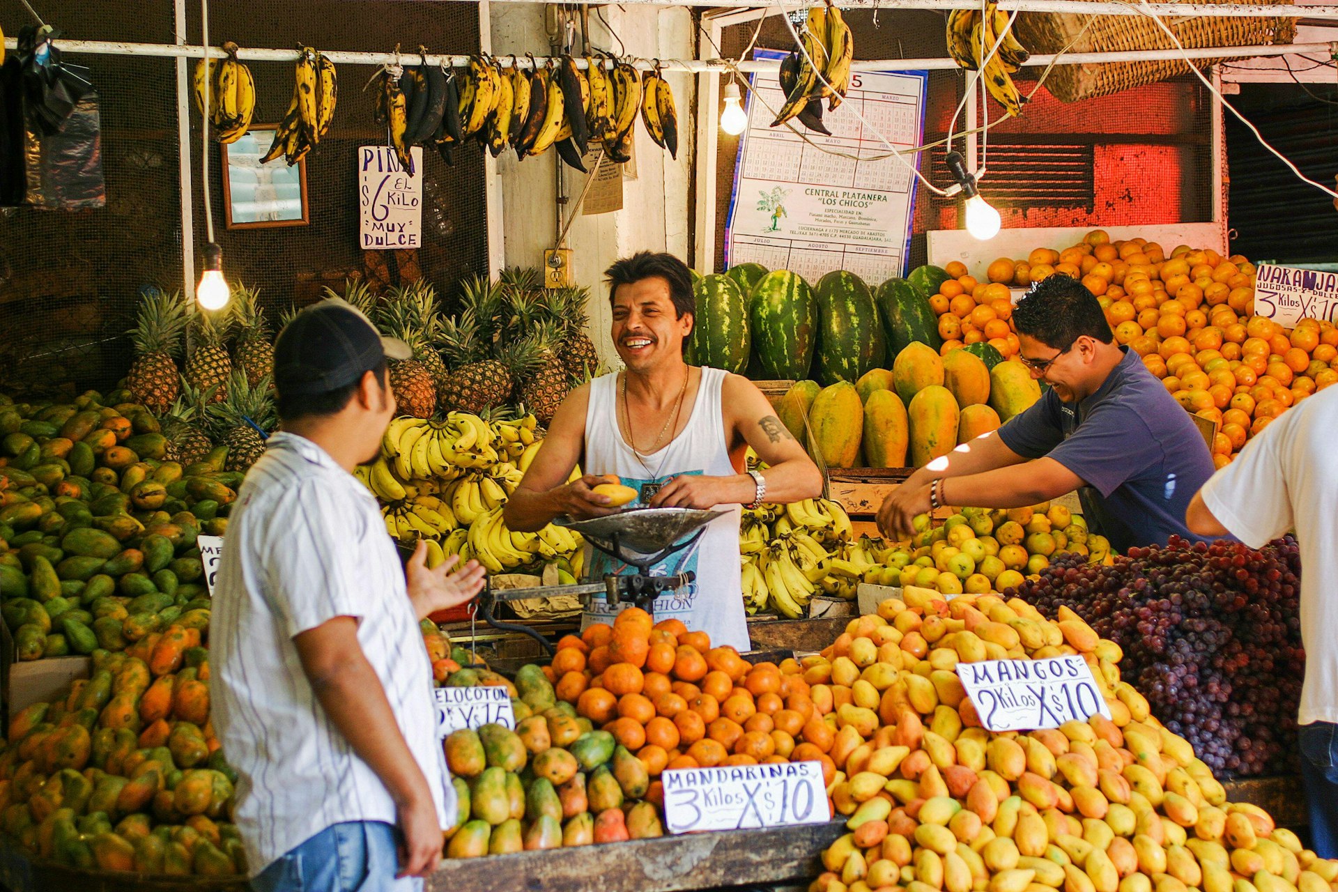 Two men share a joke as they work at a market fruit stall selling mangos, bananas and pineapples.
