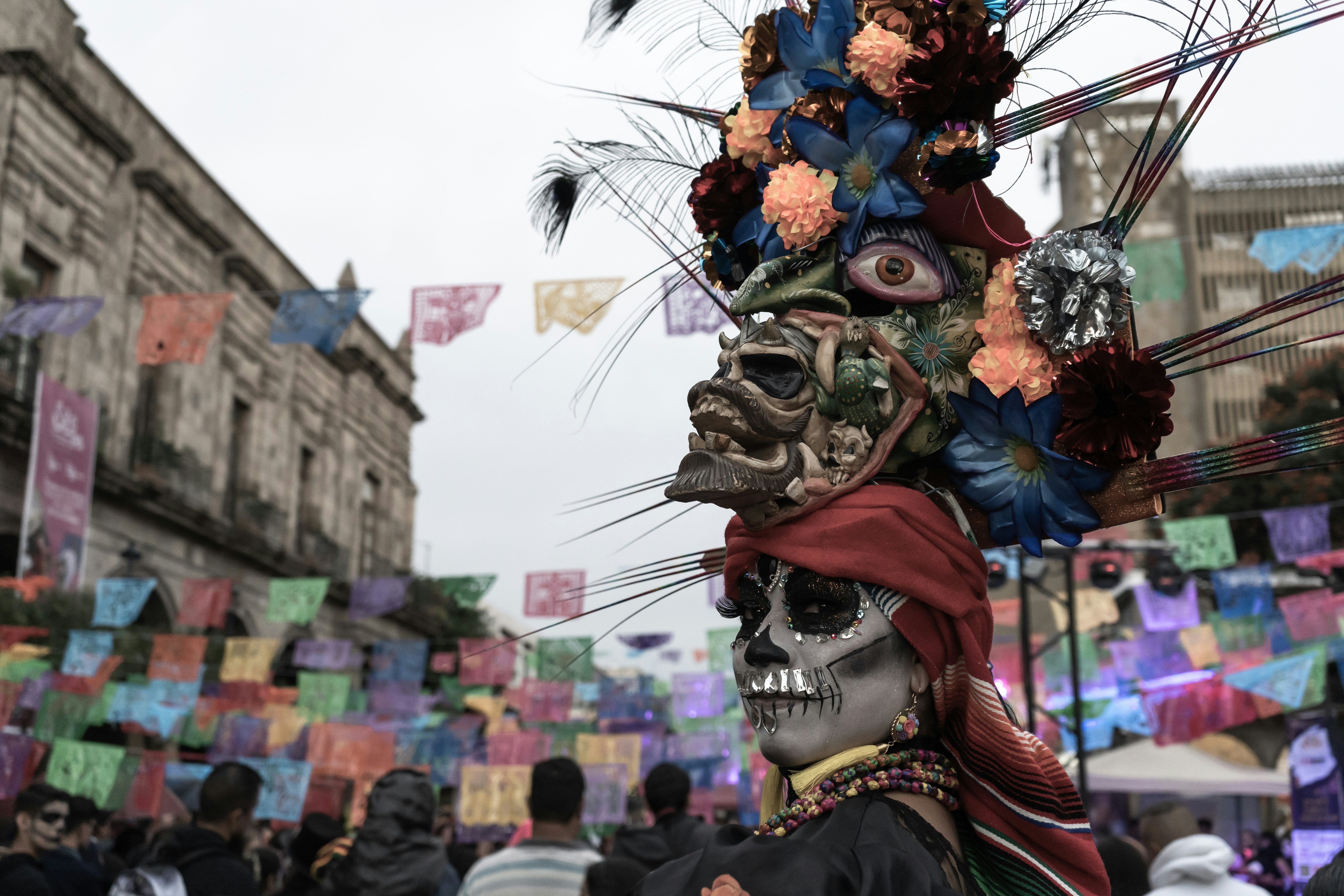 A woman has her face painted like a skull and wears an intricate head-dress made of skulls and flowers