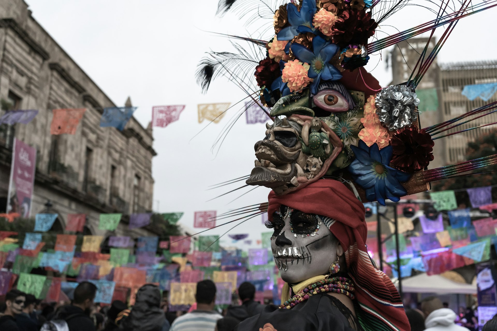 A woman has her face painted like a skull and wears an intricate head-dress made of skulls and flowers
