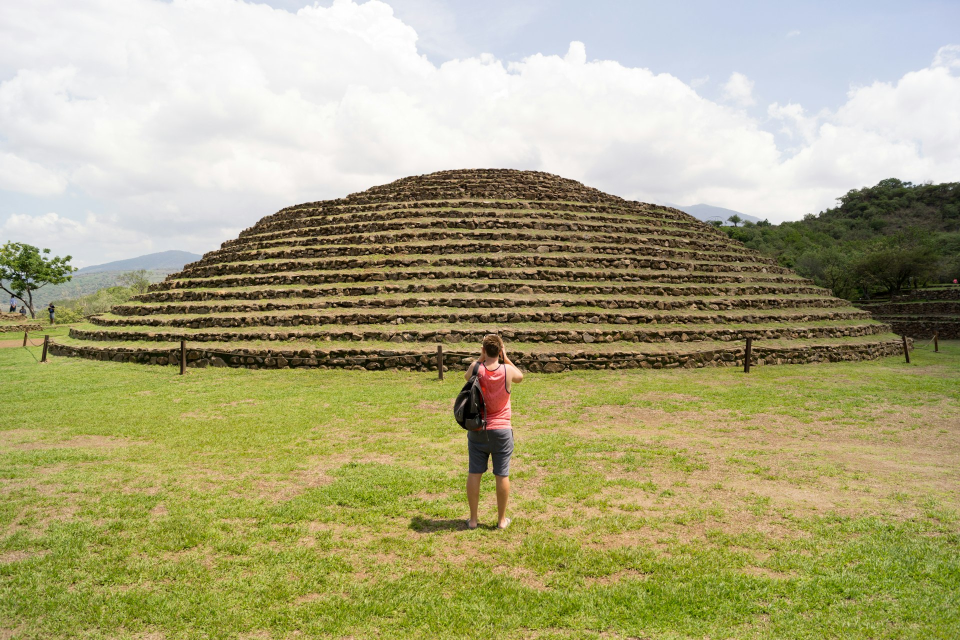 A tourist looks up at the Guachimontones ruins, a pyramid-like structure covered in green moss