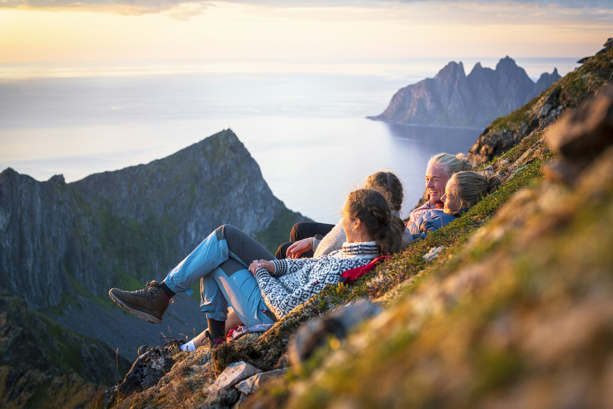 Scandinavian girls having fun lying on mountain ridge at sunset, Senja island, Troms county, Norway