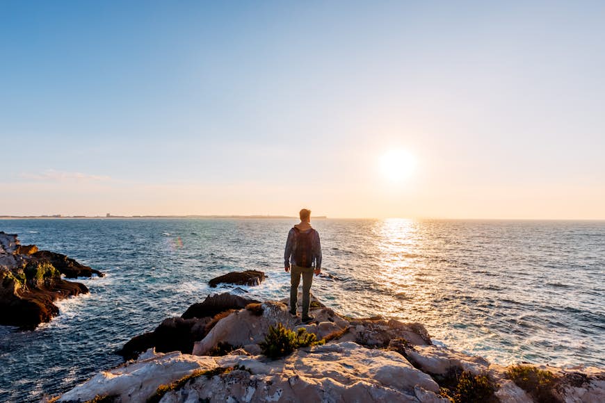 Young man standing on a cliff and looking at the sunset by the ocean on Praia Baleal, Portugal, Europe