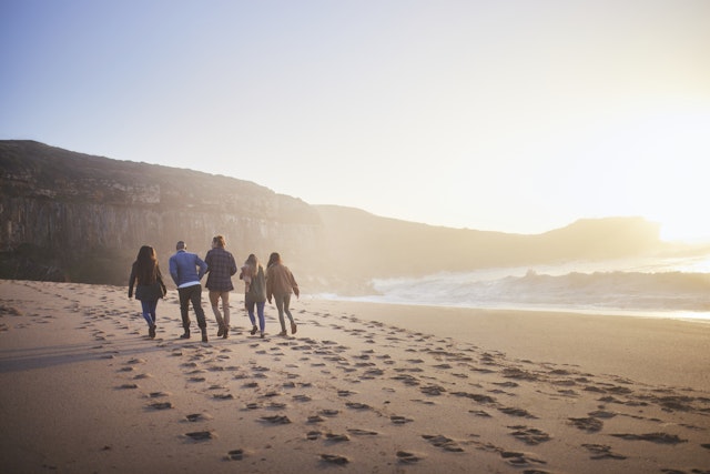 Group of friends walking together on the beach at sunset