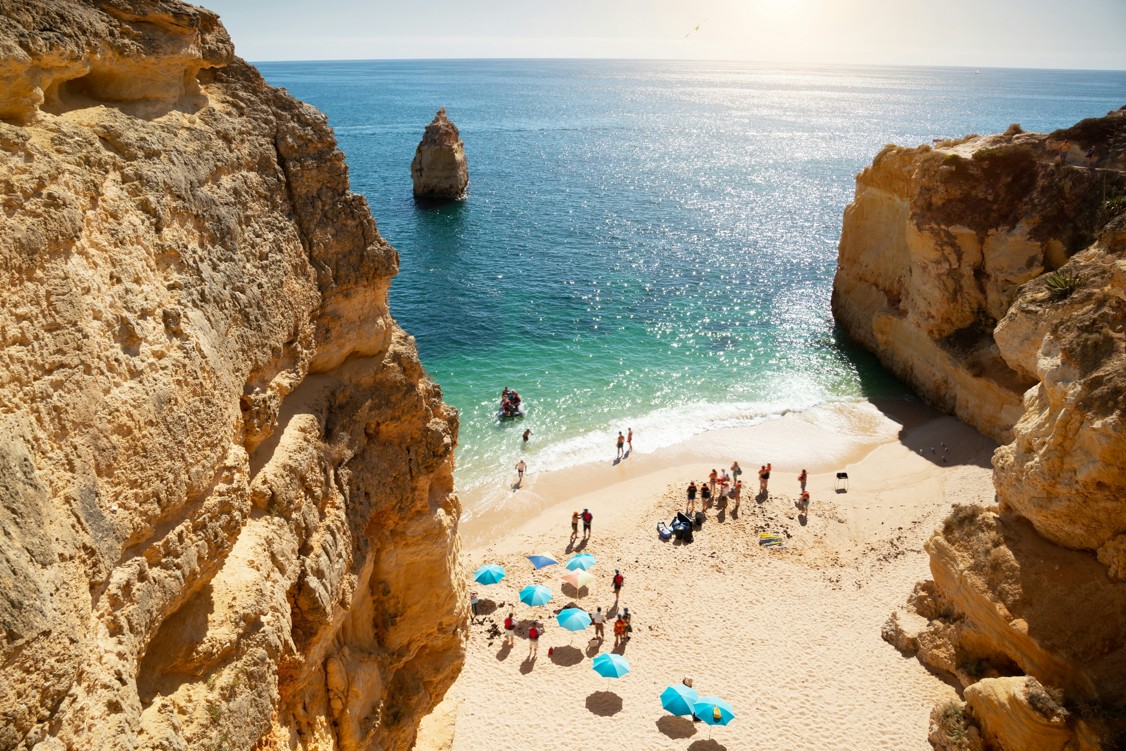 A sandy beach in a sheltered cove with people relaxing under colorful beach umbrellas