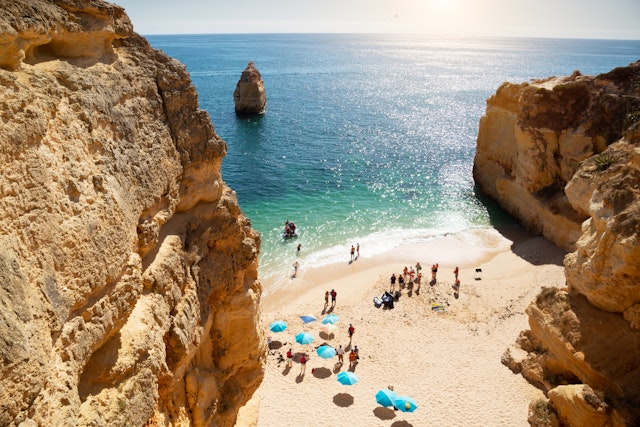A sandy beach in a sheltered cove with people relaxing under colorful beach umbrellas