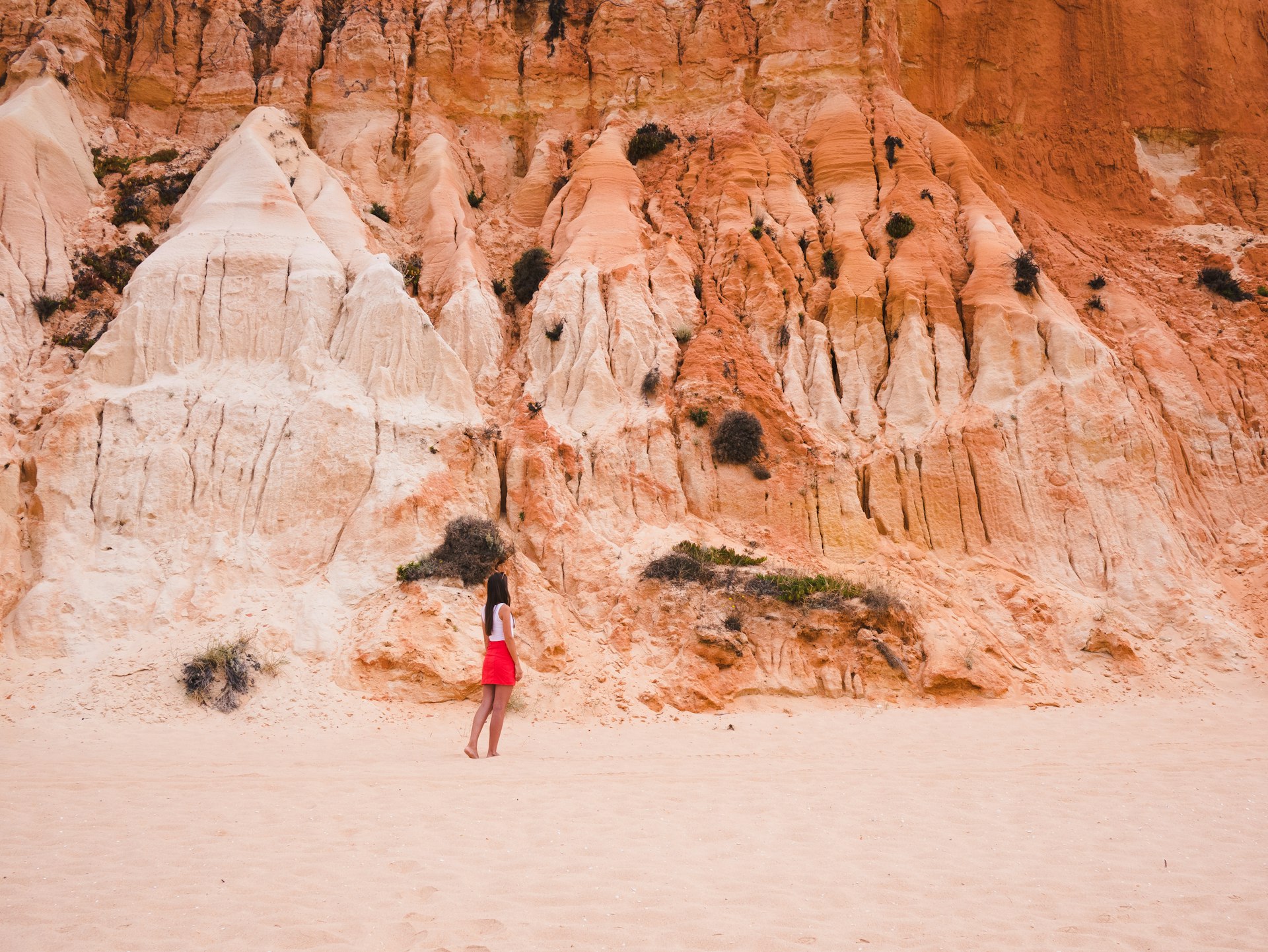 A woman walks on the sand in front of a high cliff at Praia da Falésia beach, the Algarve, southern Portugal, Europe