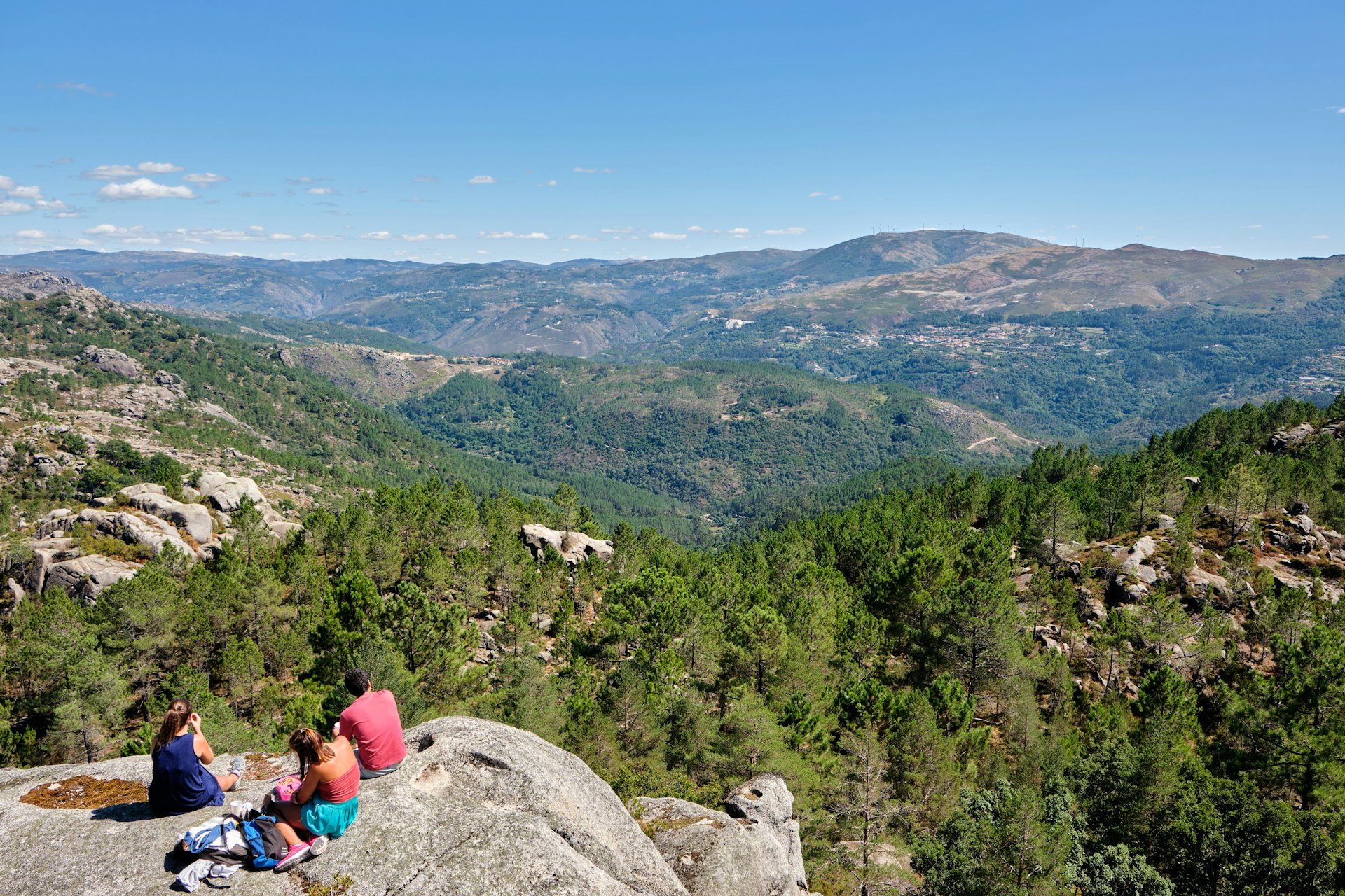 Hikers rest on a rocky outcrop overlooking forested mountains at Peneda-Gerês National Park, Gerês, Portugal, Europe