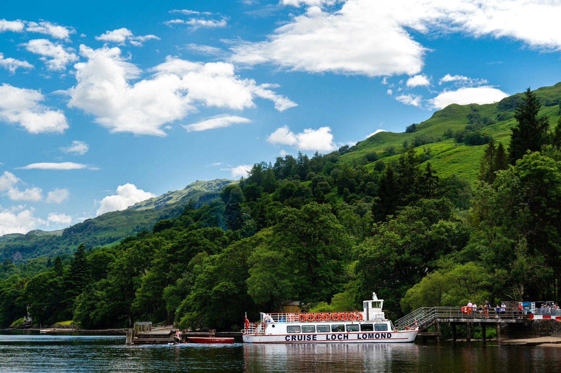 Passengers wait on a wooden jetty to board a cruise boat that crosses Loch Lomond in Scotland