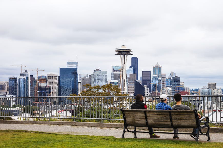 Three people sit on a bench looking out at the Seattle Skyline