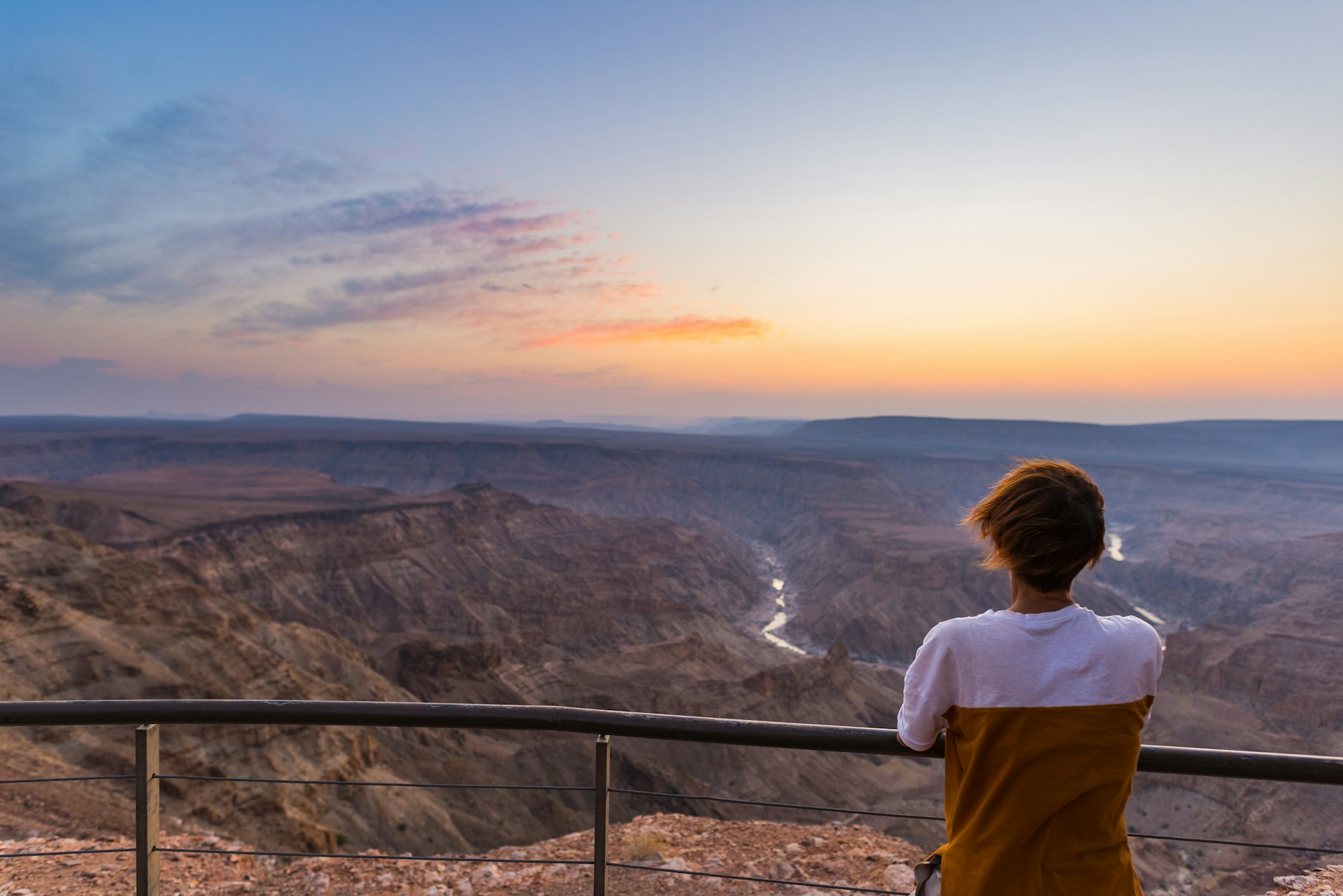 A wide-angle view of a tourist at sunset looking at the Fish River Canyon, Namibia