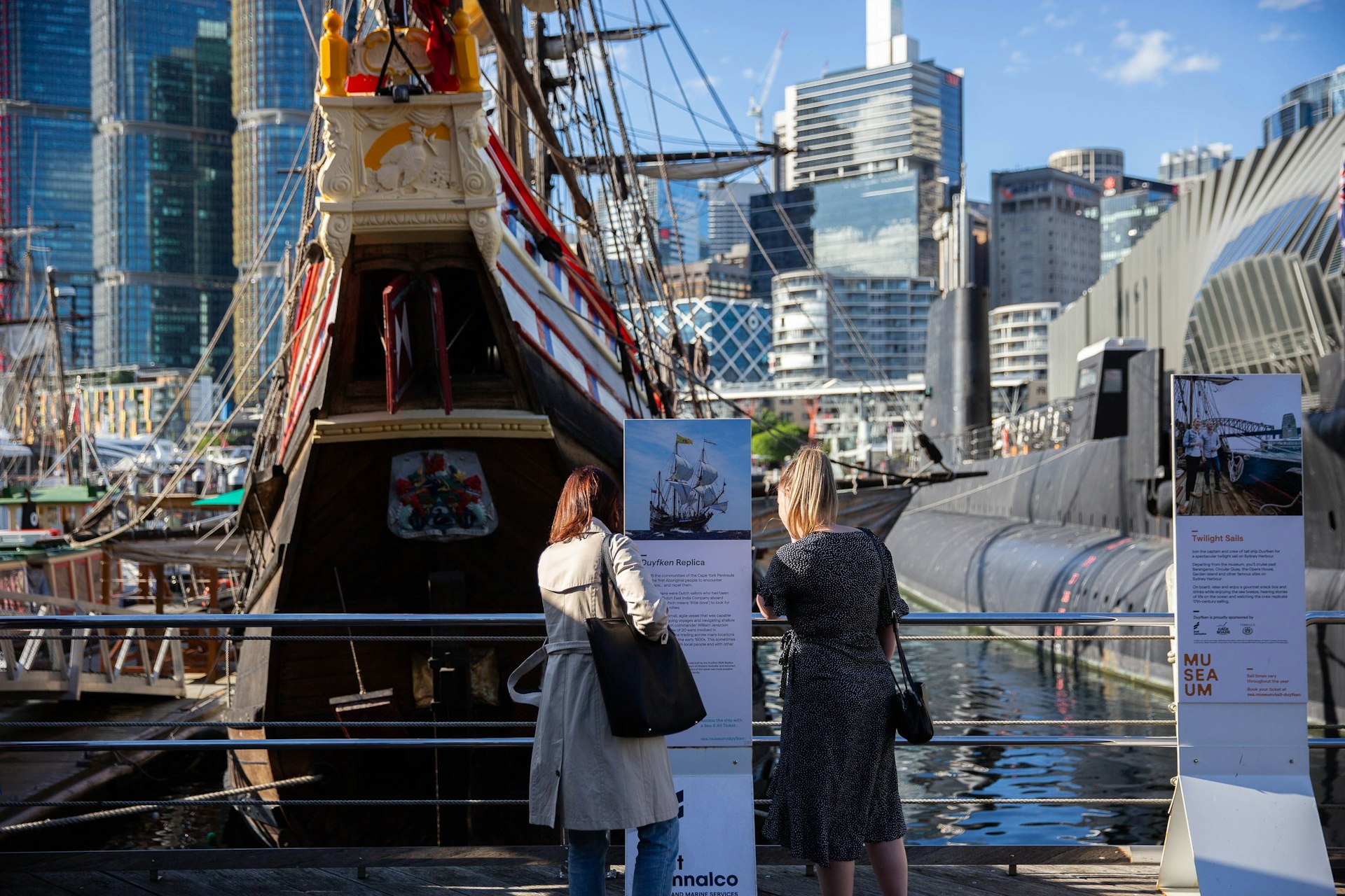 Two women stand on a dock in front of a an old wooden ship outside the Australian National Maritime Museum