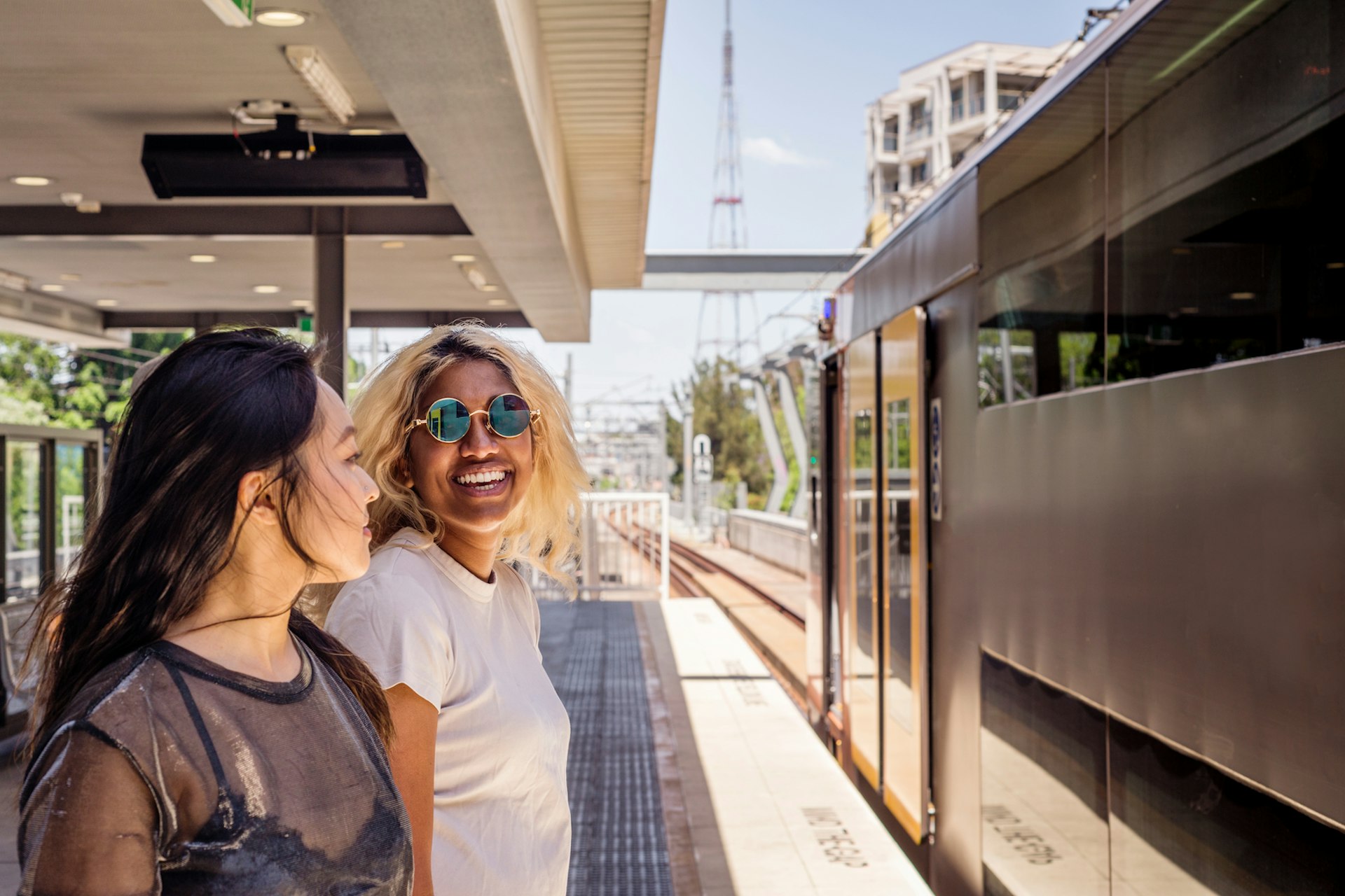 Two people share a joke and smile as they wait on a train platform