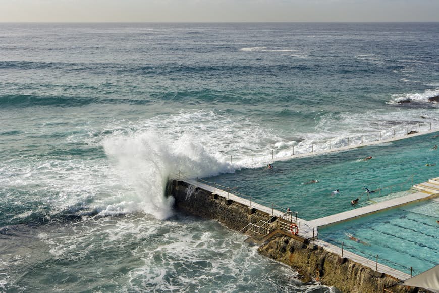An ocean wave splashes over the edge of an artificial swimming pool