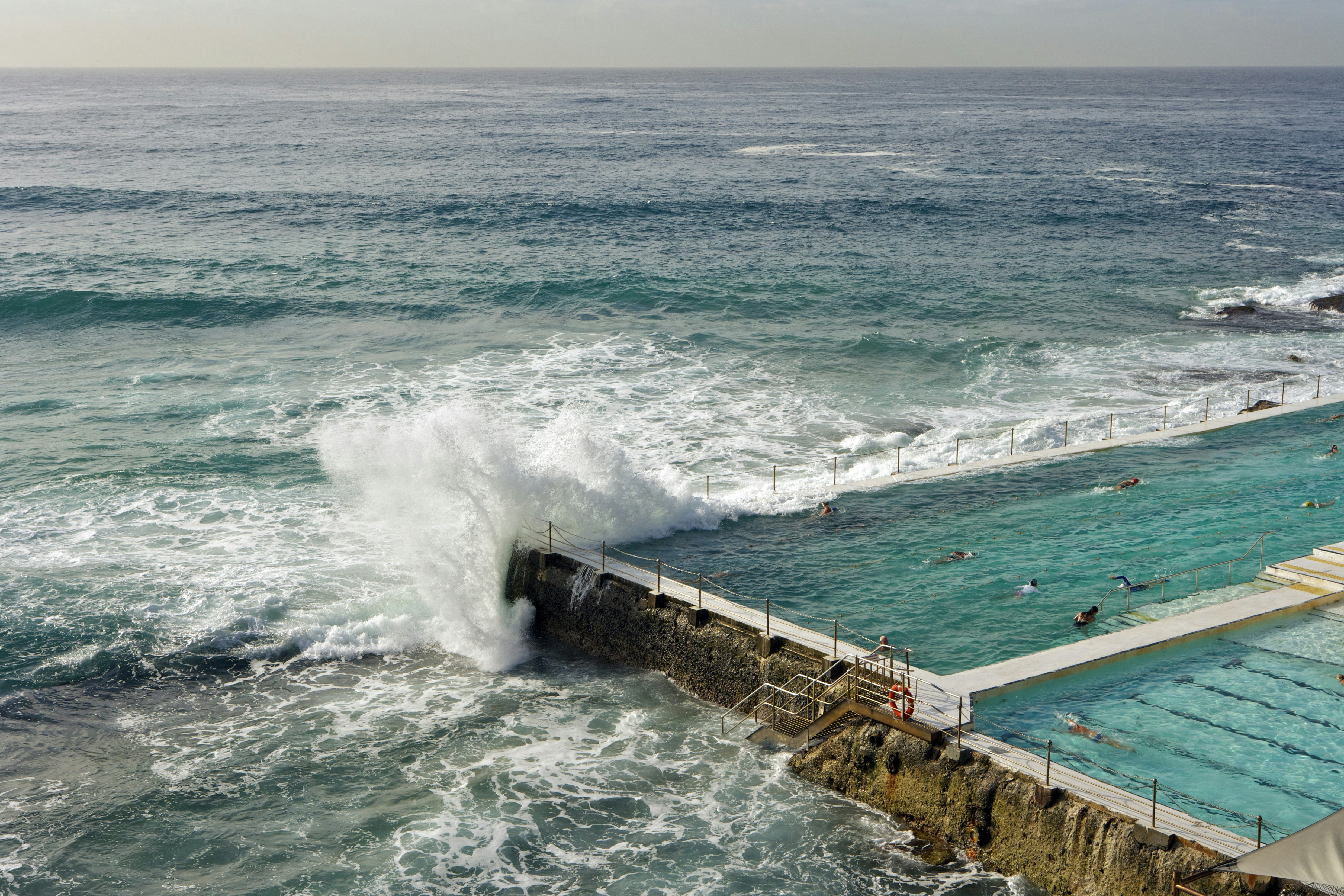 An ocean wave splashes over the edge of an artificial swimming pool