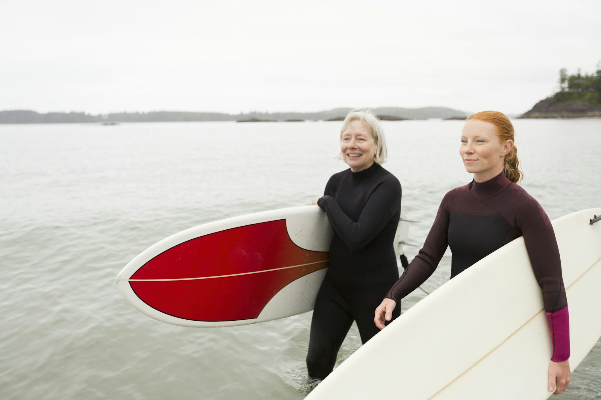Two surfers carrying boards walk along a beach smiling