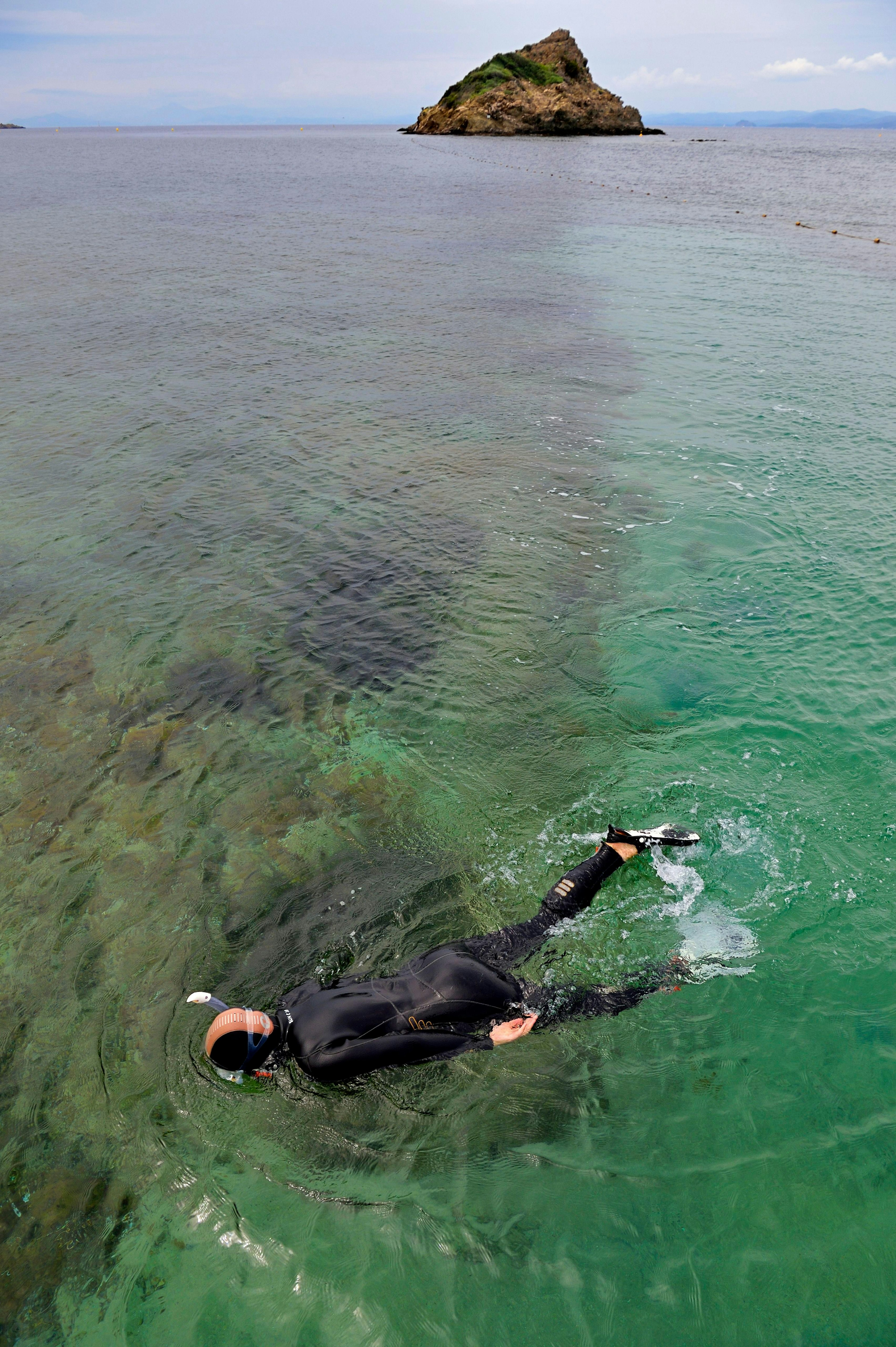 A person snorkels with the Iles d'Hyeres in the background