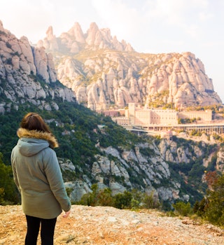 Traveler woman contemplating the monastery of Montserrat between the stunning rock formations mountain in Catalonia. - stock photo
The monastery of Montserrat from height is a famous attraction in Catalonia for the spirituality place and also for the unique black Virgin Mary surrounded by stunning mountains.