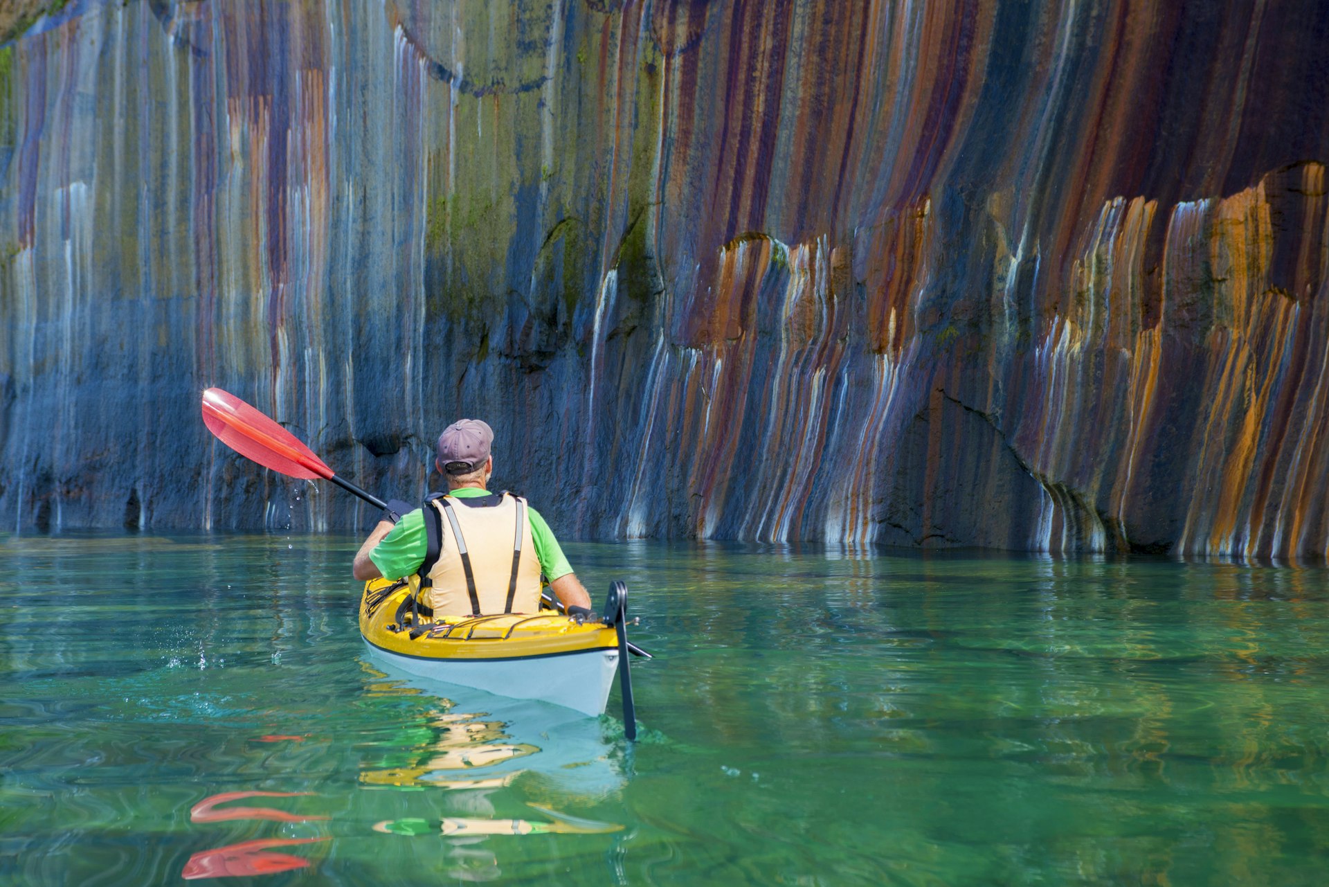 A man in a kayak approaches the multi-colored cliffs at Pictured Rocks National Lakeshore, Lake Superior, Upper Peninsula, Michigan, USA