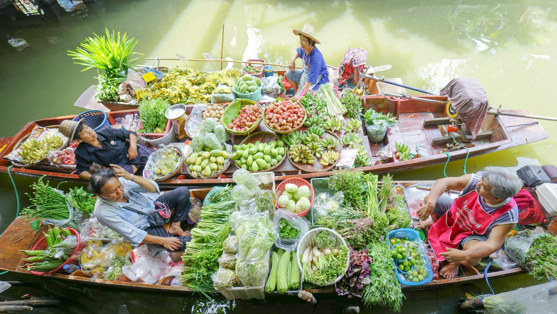 Floating market traders with fruits and vegetables packed into small boats in a Bangkok canal, Taling Chan 