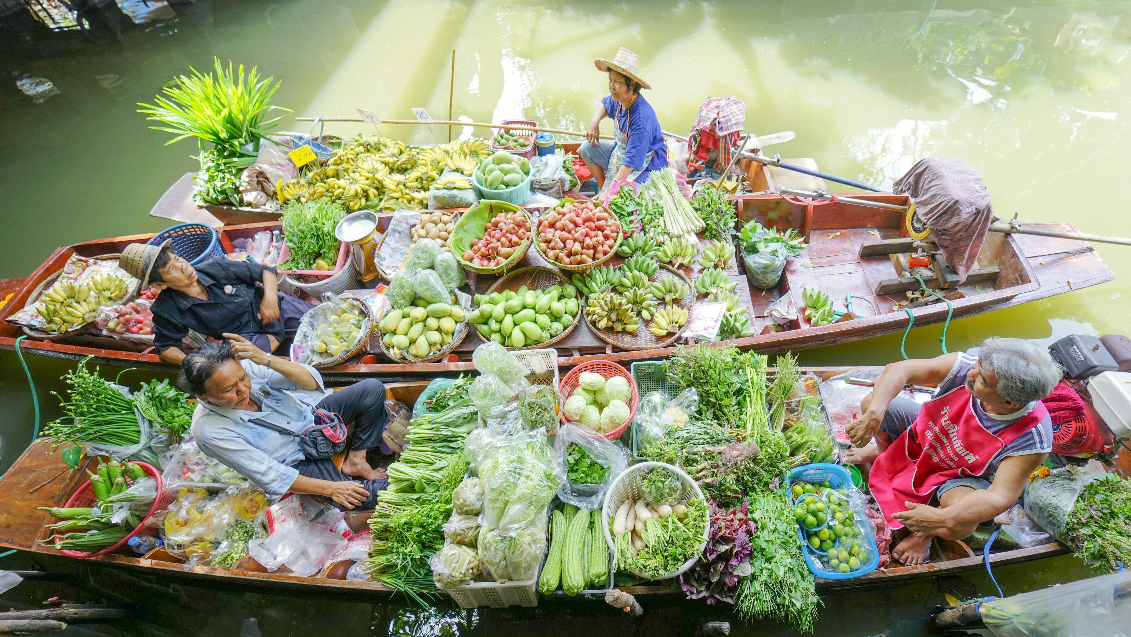 Floating market traders with fruits and vegetables packed into small boats in a Bangkok canal, Taling Chan