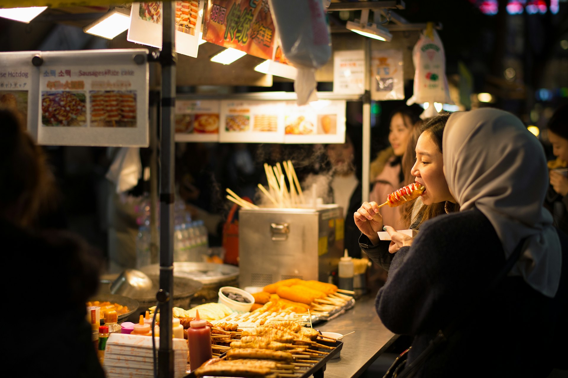 Women eating fish cakes and hot dogs, Myeong-dong, Seoul, South Korea