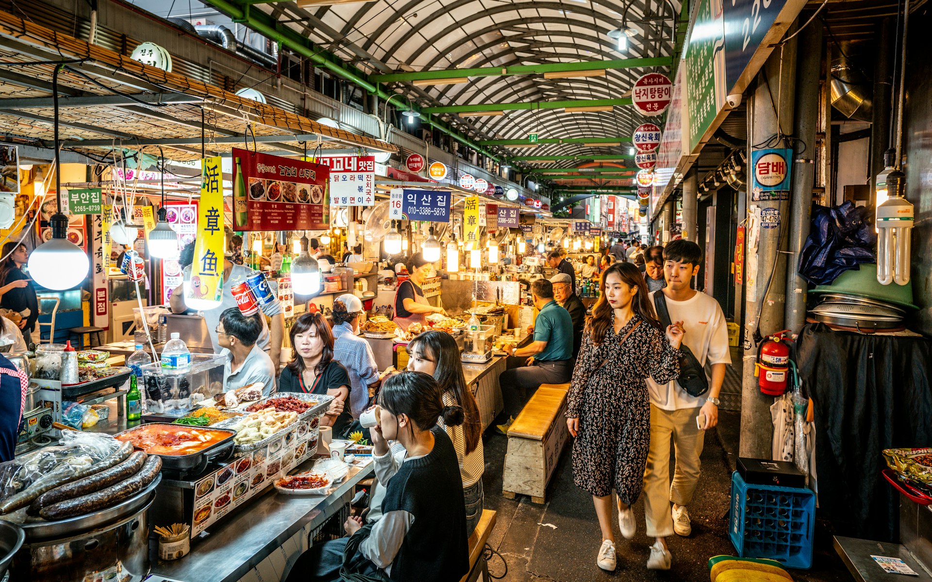 View of an alley of the Kwangjang market at night with people eating street food at stalls