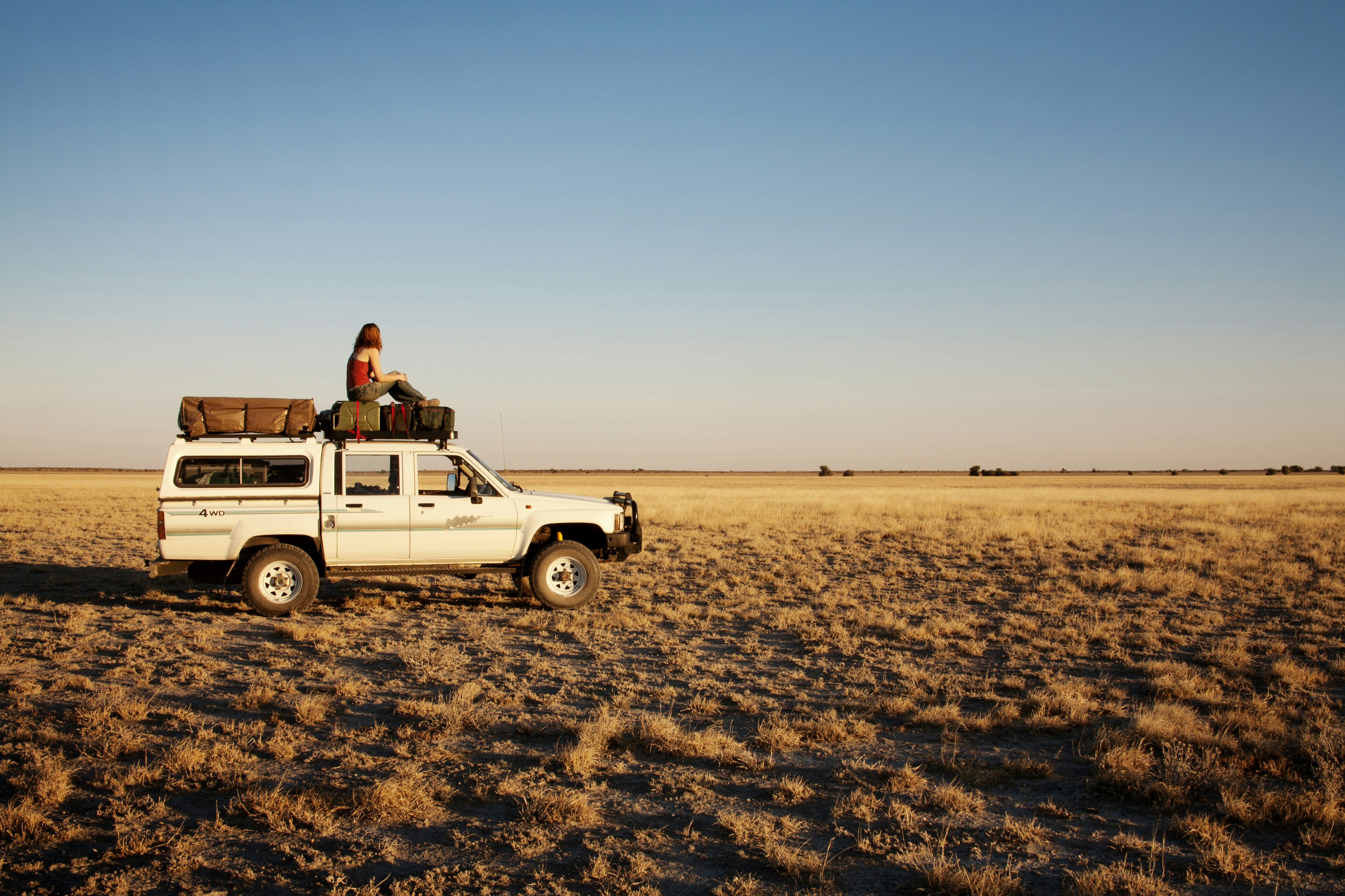 A woman sits on the roof of an off-road vehicle in open grassland