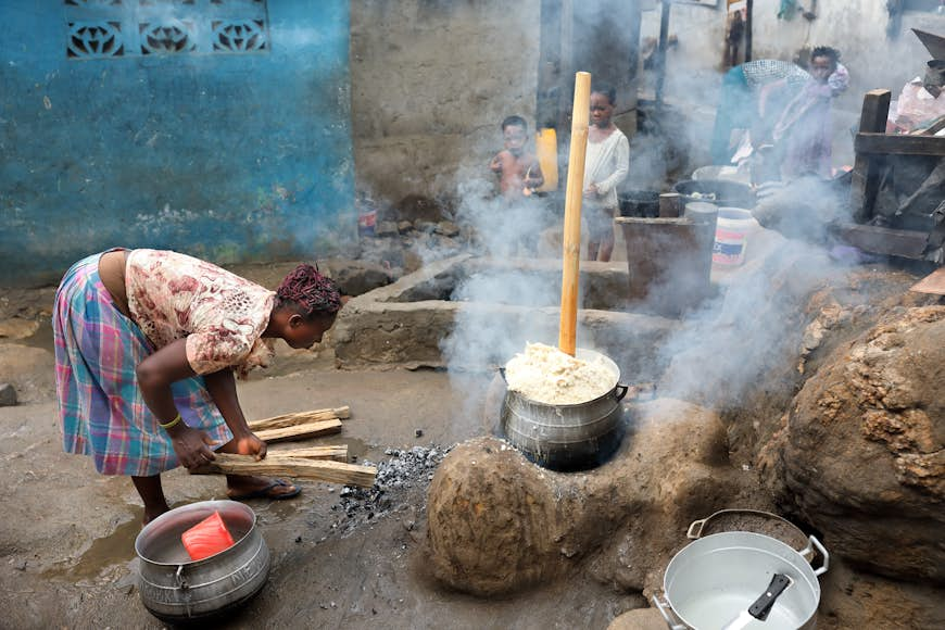 Unidentified woman prepares traditional corn porridge in a large pot outdoors