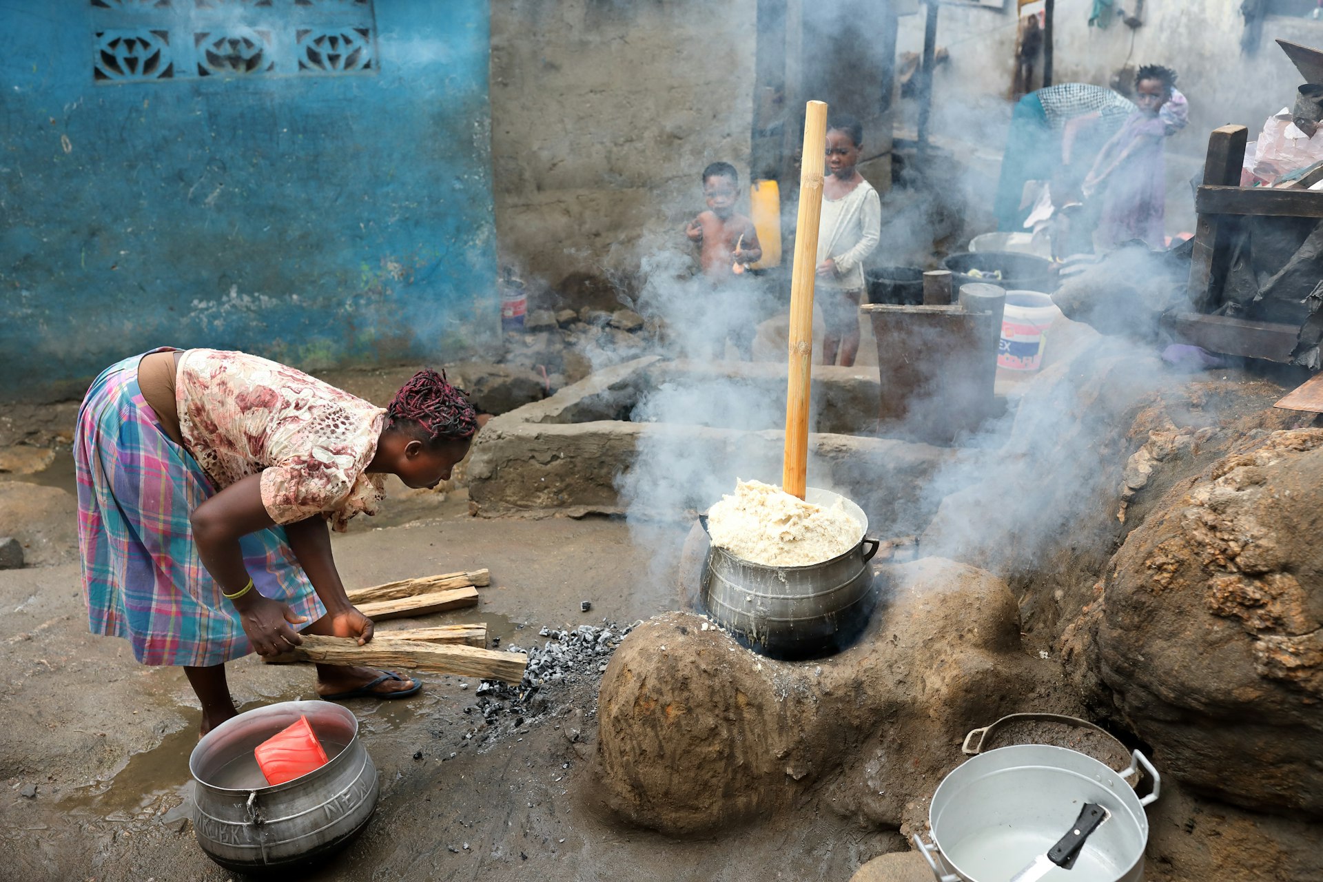 Unidentified woman prepares traditional corn porridge in a large pot outdoors