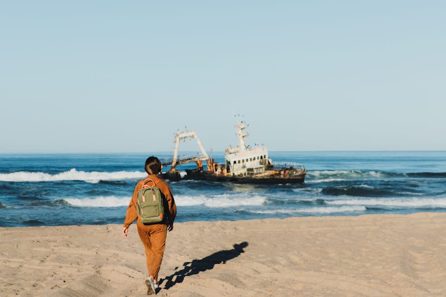 Young woman with backpack looking at an abandoned ship on the Skeleton Coast in Namibia