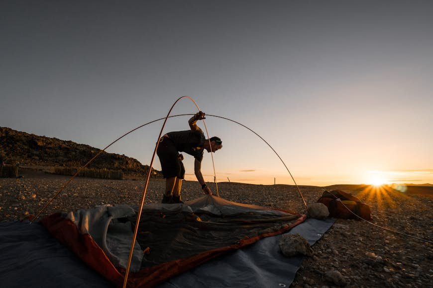 A person sets up their tent in a remote part of the African bush as the sun sets