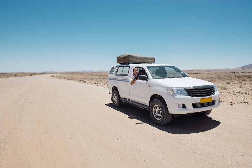Man in a four-wheel drive car with a tent on the roof parked on a dusty desert road
