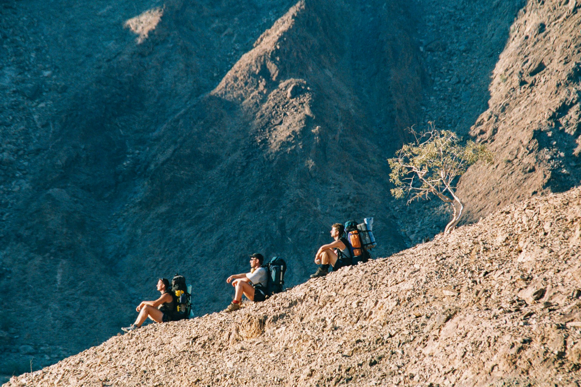 Three hikers sitting on a ridge in a mountainous arid area