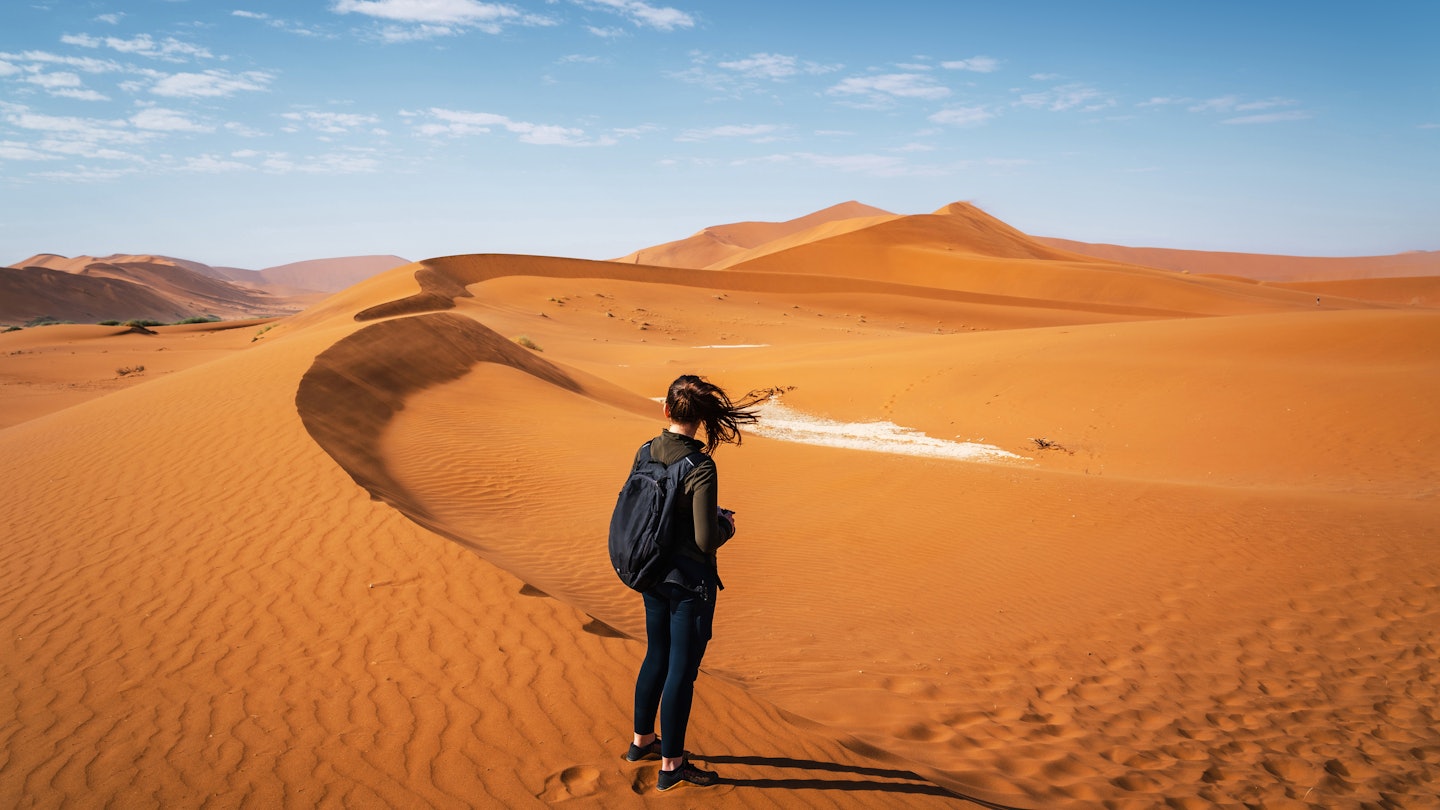 Active female traveler hiking on the dunes around Deadvlei in the Namib Desert, Namib-Naukluft National Park, Namibia, Africa.