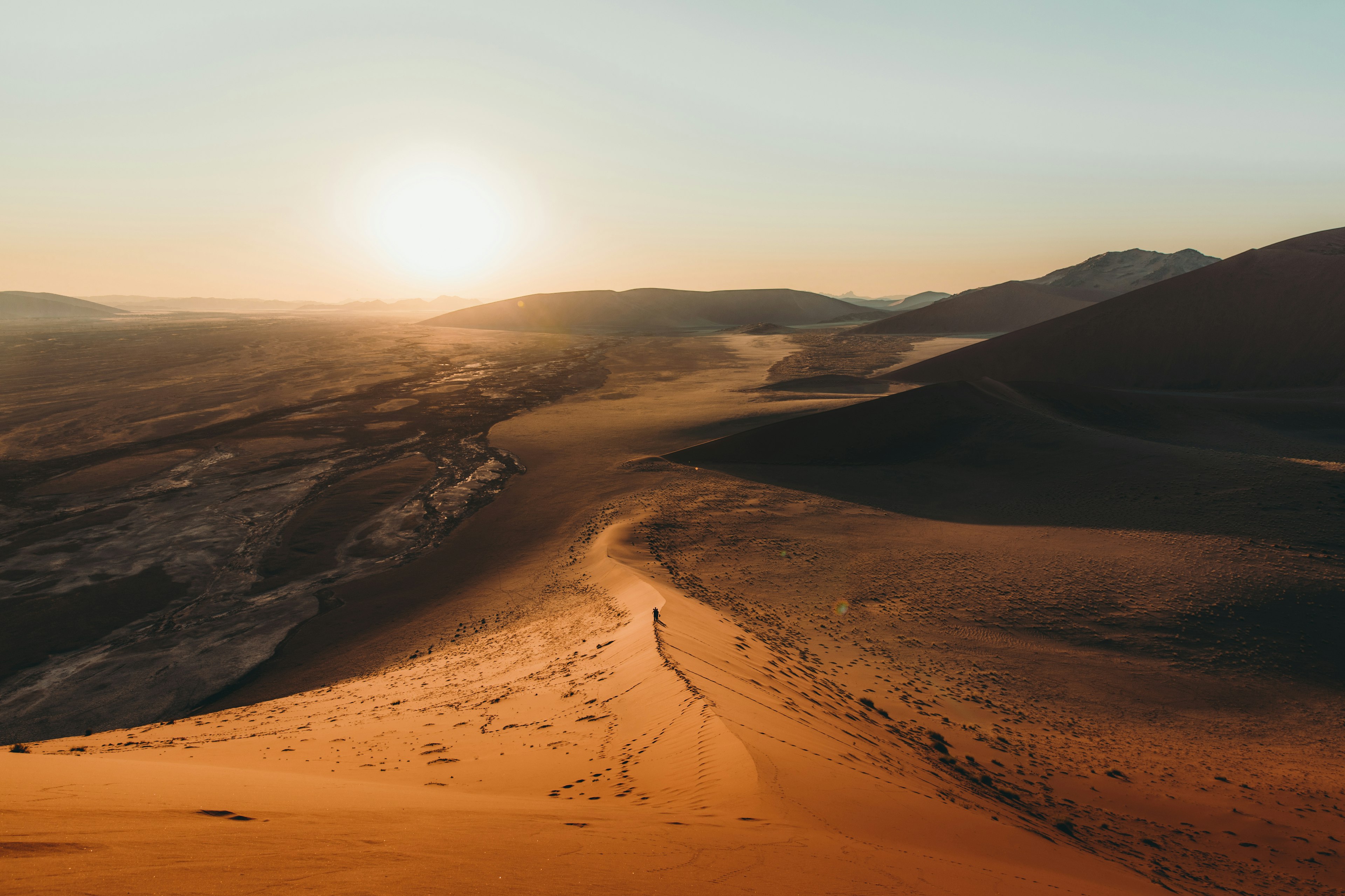 A solo shadowy figure on vast red sand dunes in the Namibian desert