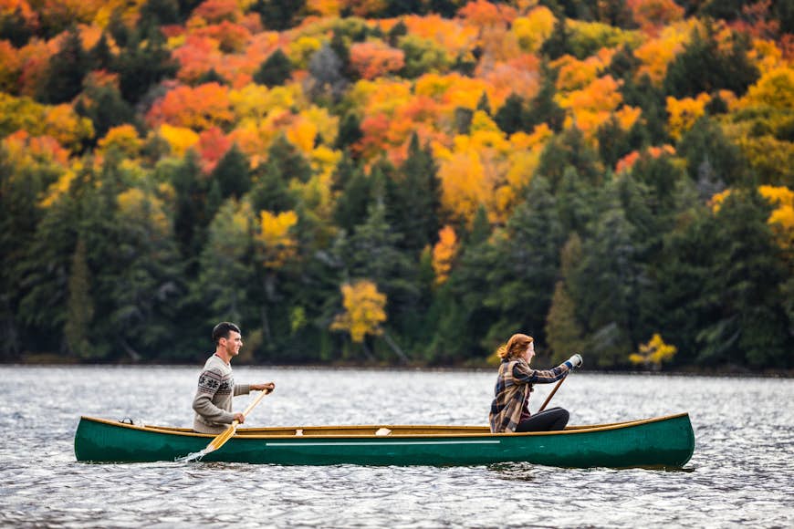 Par som njuter av en tur på en typisk kanot i Algonquin Park, Ontario - Kanada, med höstlövverk i bakgrunden