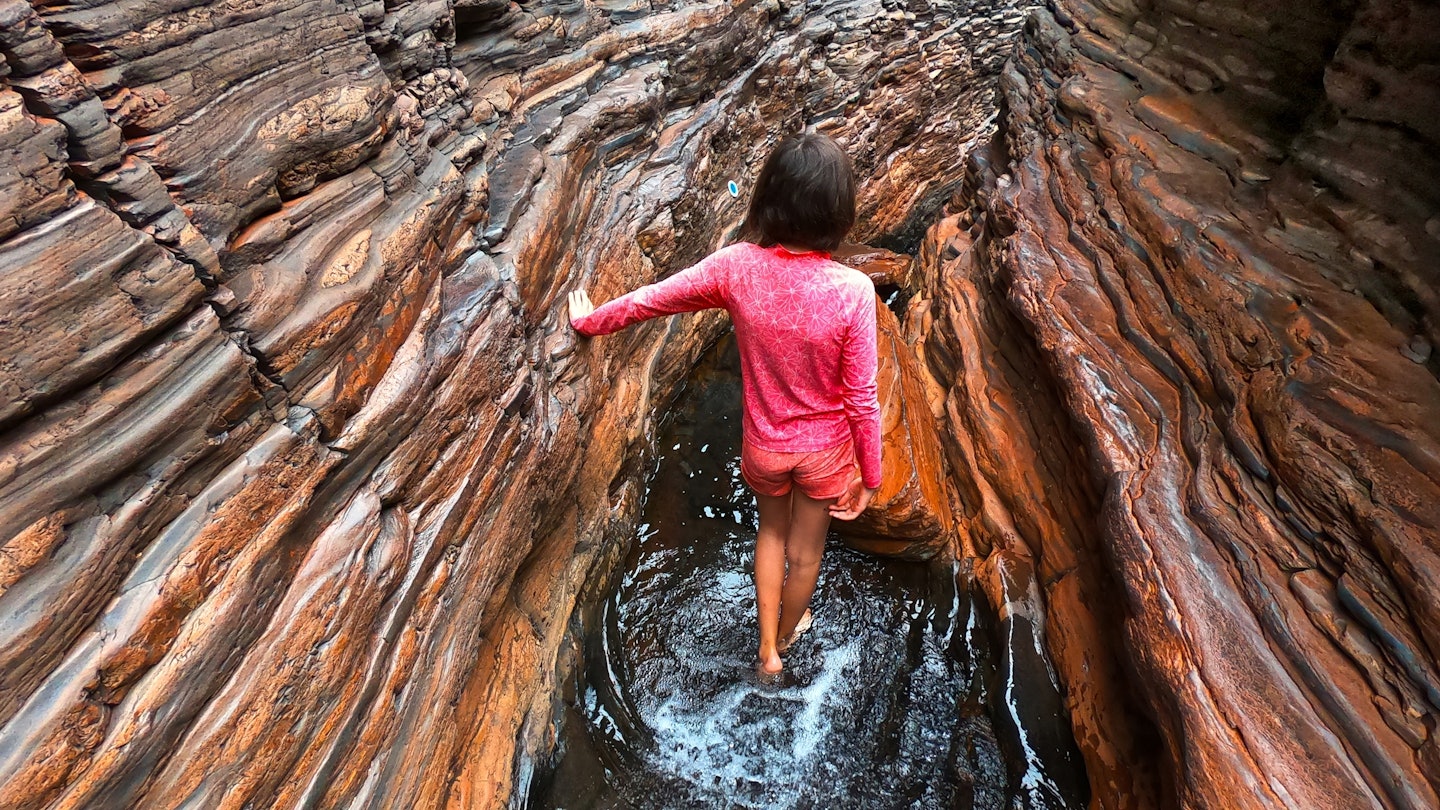 Rear view of a young adult Australian woman hiking at spider walk at Hancock Gorge in Karijini National Park Pilbara region in Western Australia; Shutterstock ID 2179893099; your: Sloane Tucker; gl: 65050; netsuite: Online Editorial; full: Western Australia Article