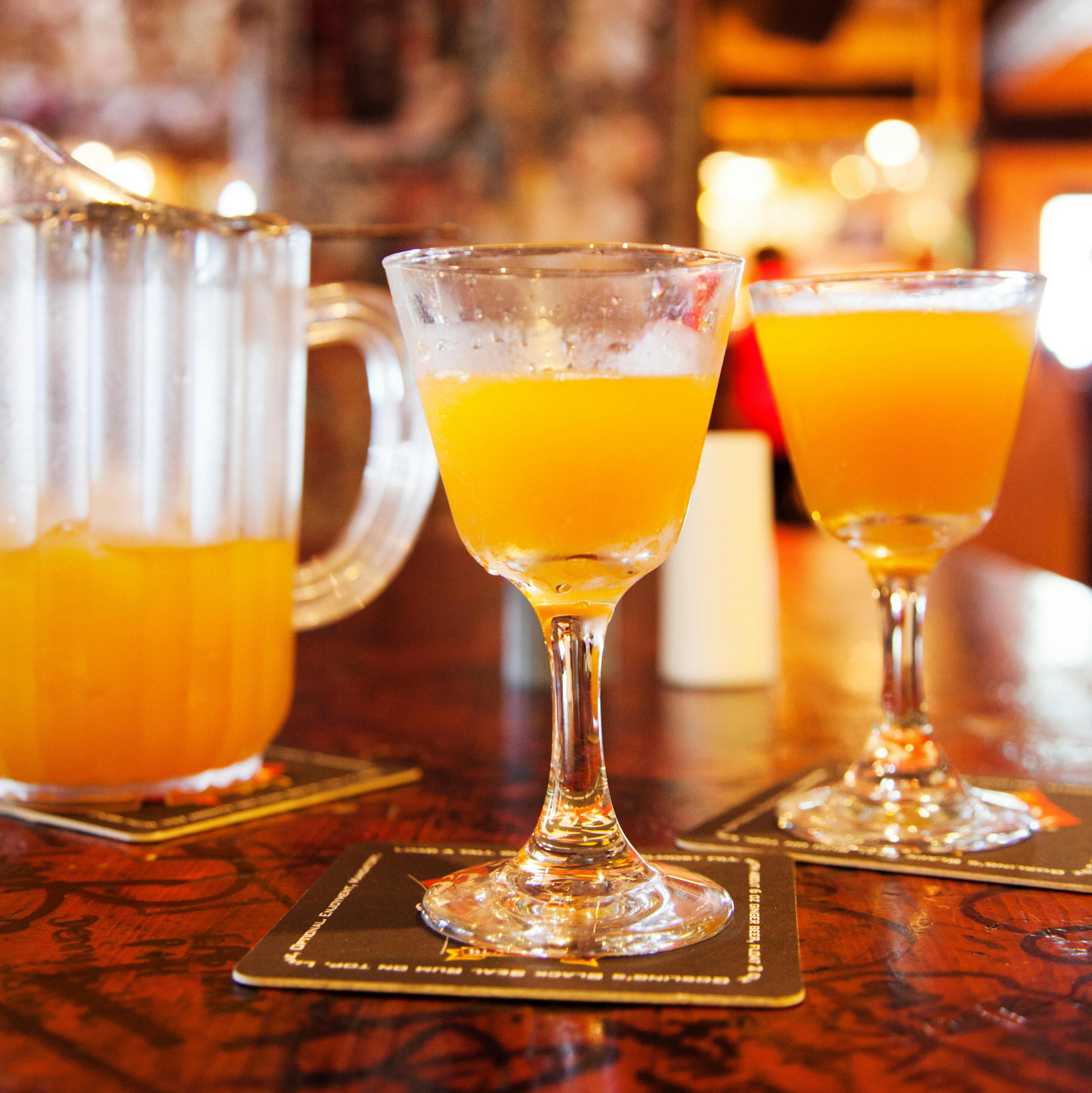 A yellow cocktail in a glass on a bar.