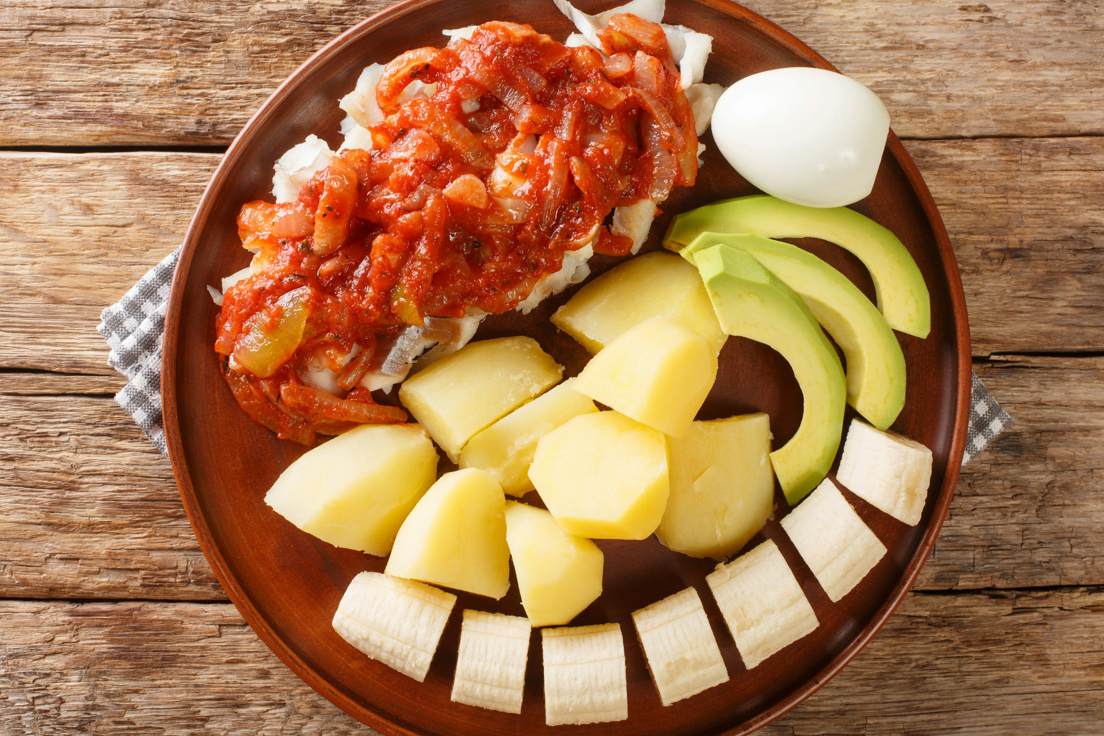 Bermuda codfish breakfast with onion tomato sauce, boiled potatoes, eggs, banana and avocado on a plate