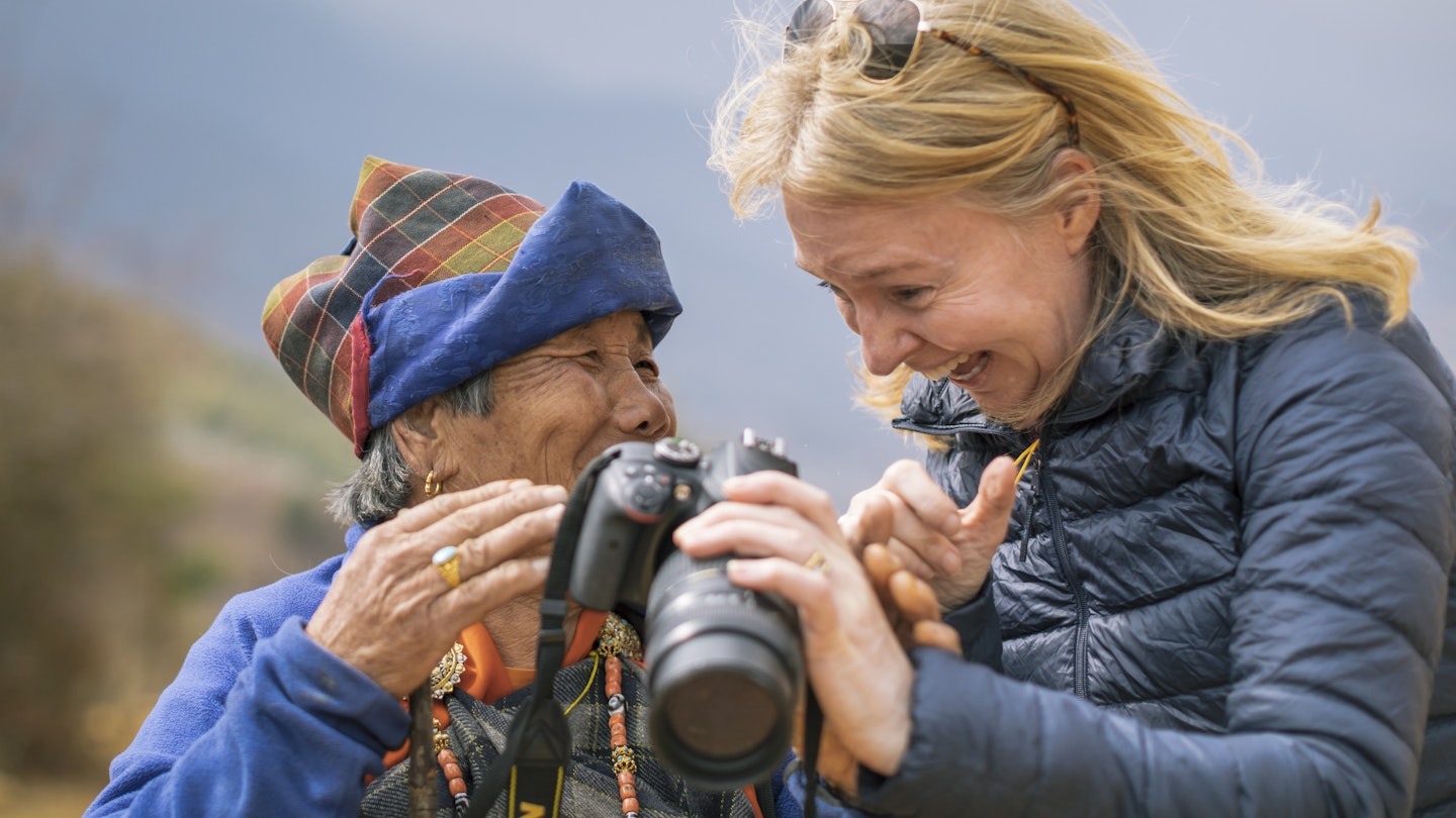 A female tourist has taken a photo of an elderly Bhutanese woman and is now showing the woman that photo on the screen on the back of the camera near Dranjo Goemba - buddhist monastery and school in the uper Paro Valley