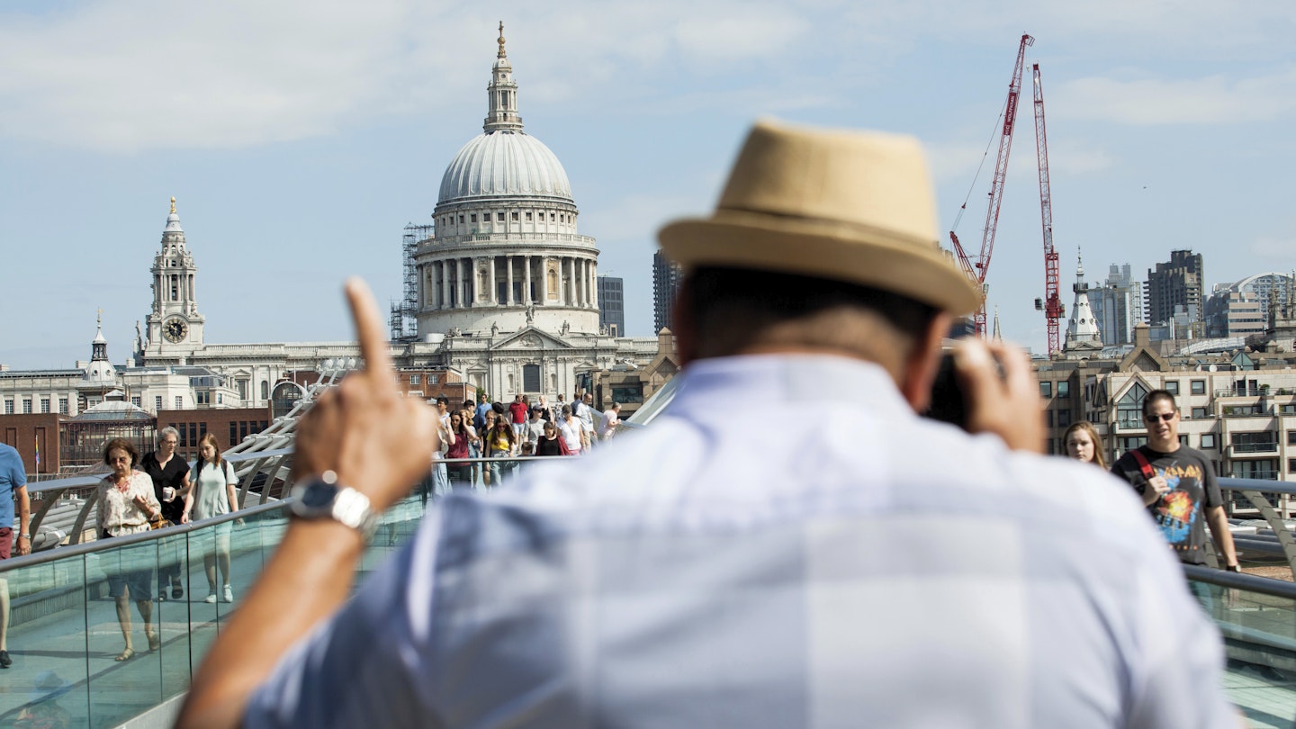 A man takes a photo of Millennium Bridge, with St Paul's Cathedral in the background.